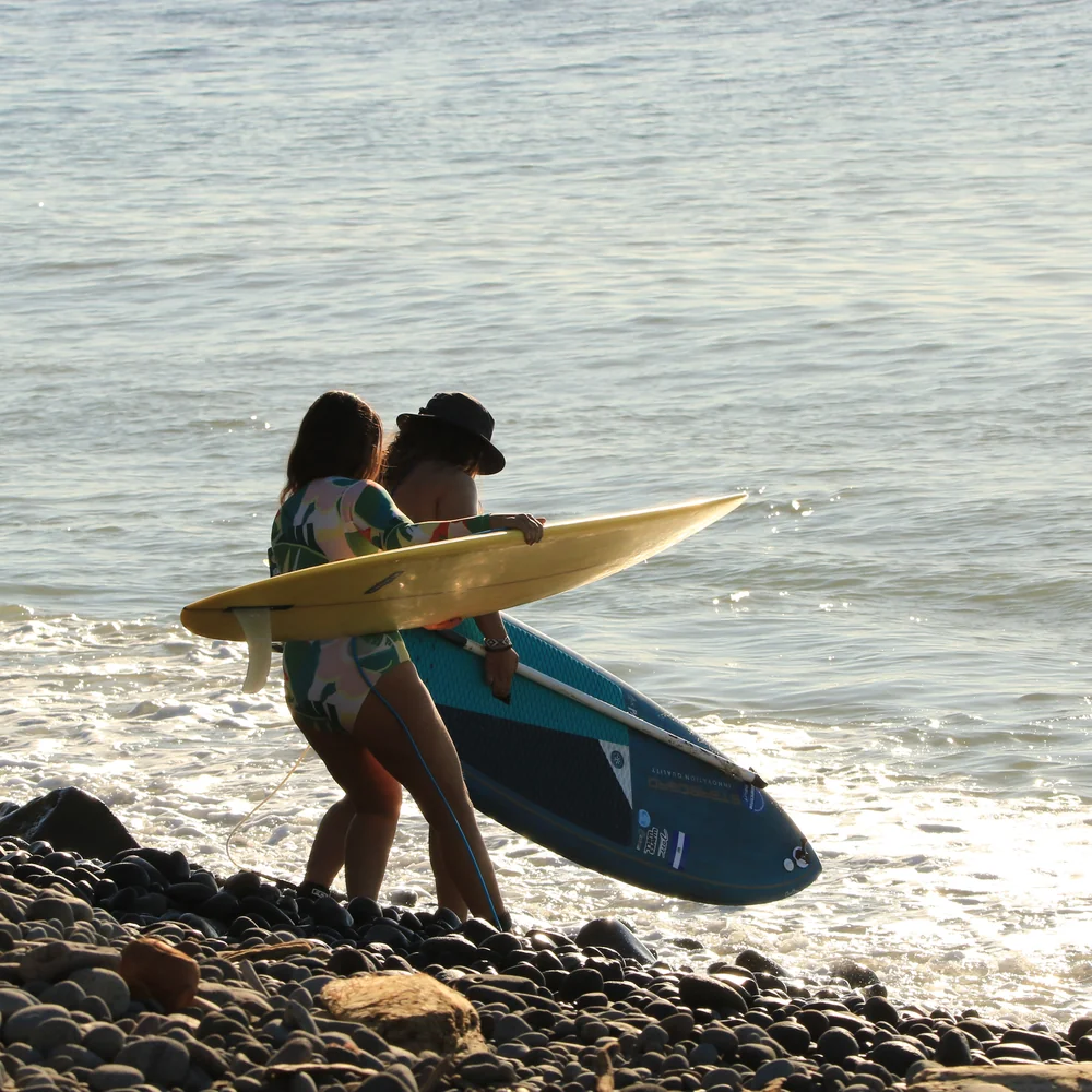 Two Waveswell guests carrying their paddle boards down to the water at golden hour