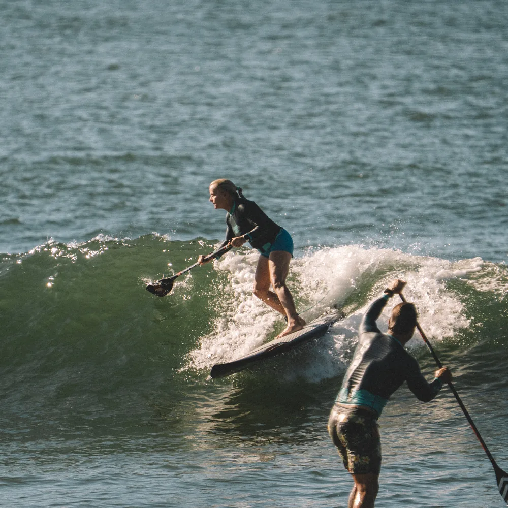 A Waveswell guest riding along the face of a wave on her paddle board in El Salvador